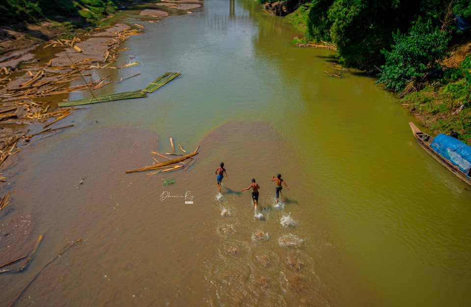Children running through a shallow river in the Hill Tracts
